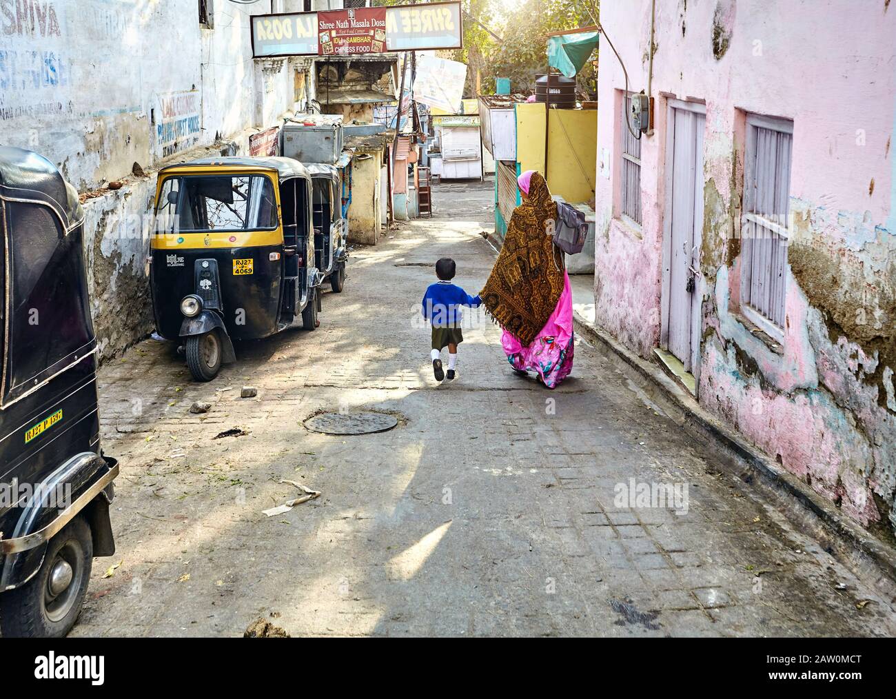 Udaipur, RAJASTHAN, INDE - 03 MARS 2015: Femme en sari rose allant à l'école avec son fils dans la rue étroite avec Rickshaw taxi à Udaipur cit Banque D'Images