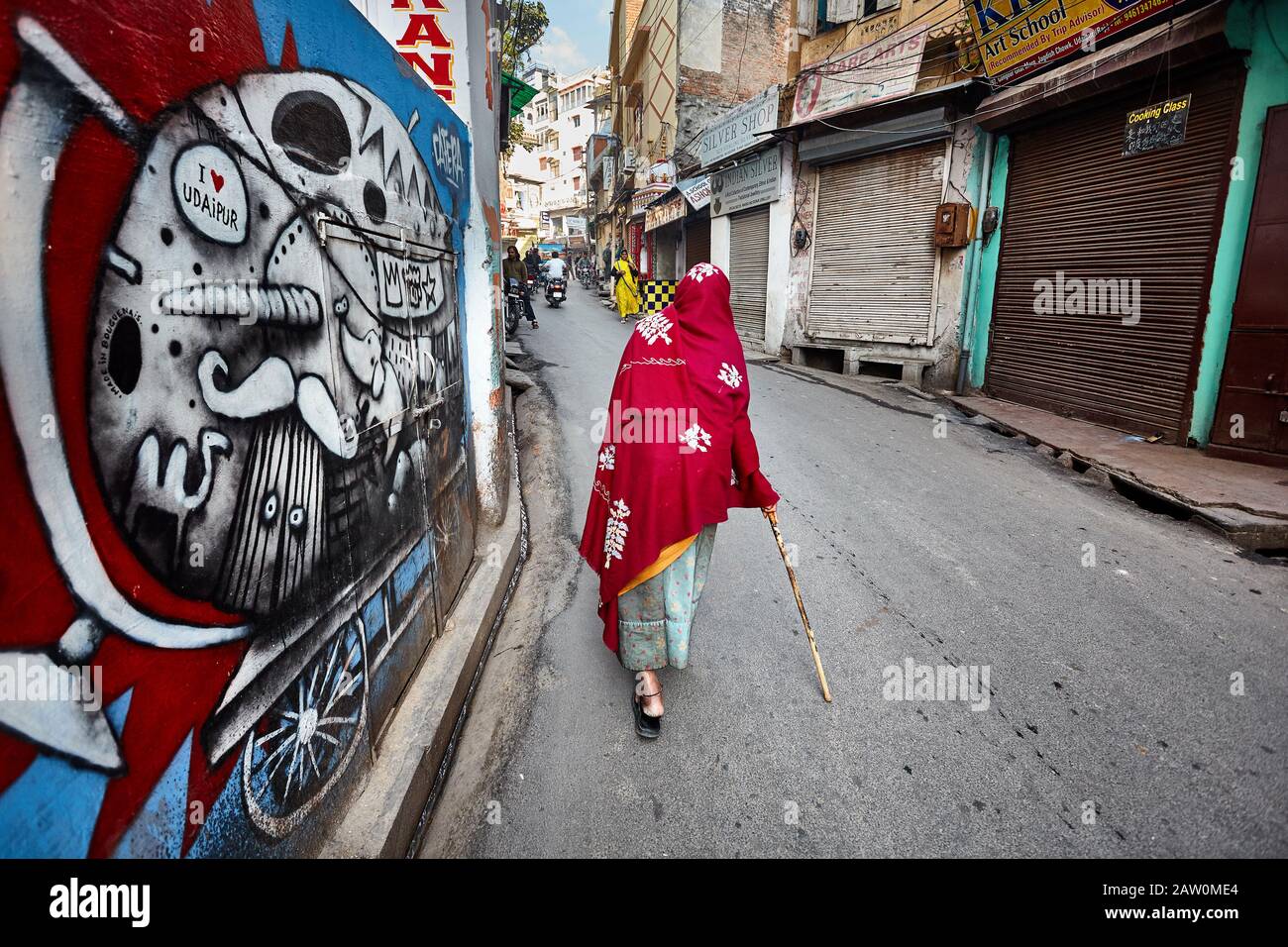 Udaipur, RAJASTHAN, INDE - 03 MARS 2015 : vieille femme dans le foulard rouge qui descend dans la rue avec des graffitis d'art moderne sur le mur dans la ville d'Udaipur. Banque D'Images