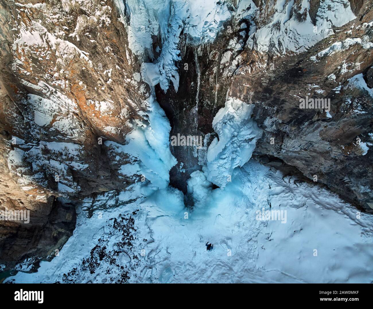 Le randonneur se trouve à proximité d'une chute d'eau gelée avec des icules dans les montagnes enneigées du Kazakhstan. Tir de drone aérien, vue de dessus. Banque D'Images