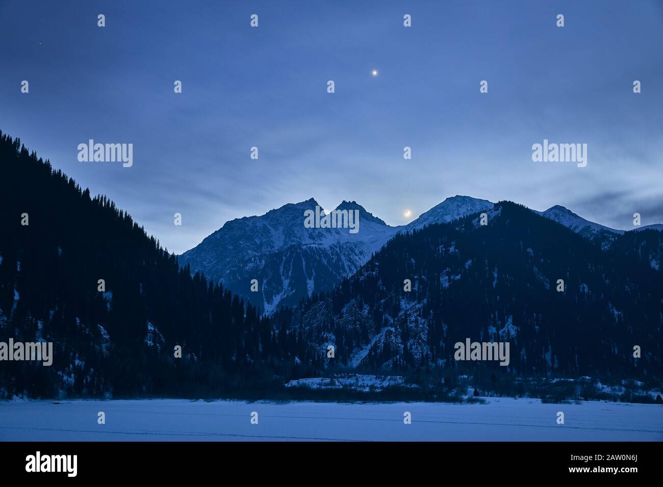 Paysage du lac gelé dans les montagnes sous ciel nocturne avec étoiles et lune. Banque D'Images