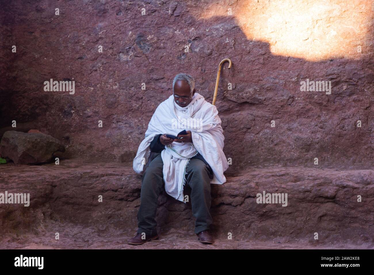 Lalibela, Ethiopie - Nov 2018: Homme vêtu de blanc traditionnel, assis à l'extérieur et lire livre de prières à côté des églises souterraines de Lalibela Banque D'Images