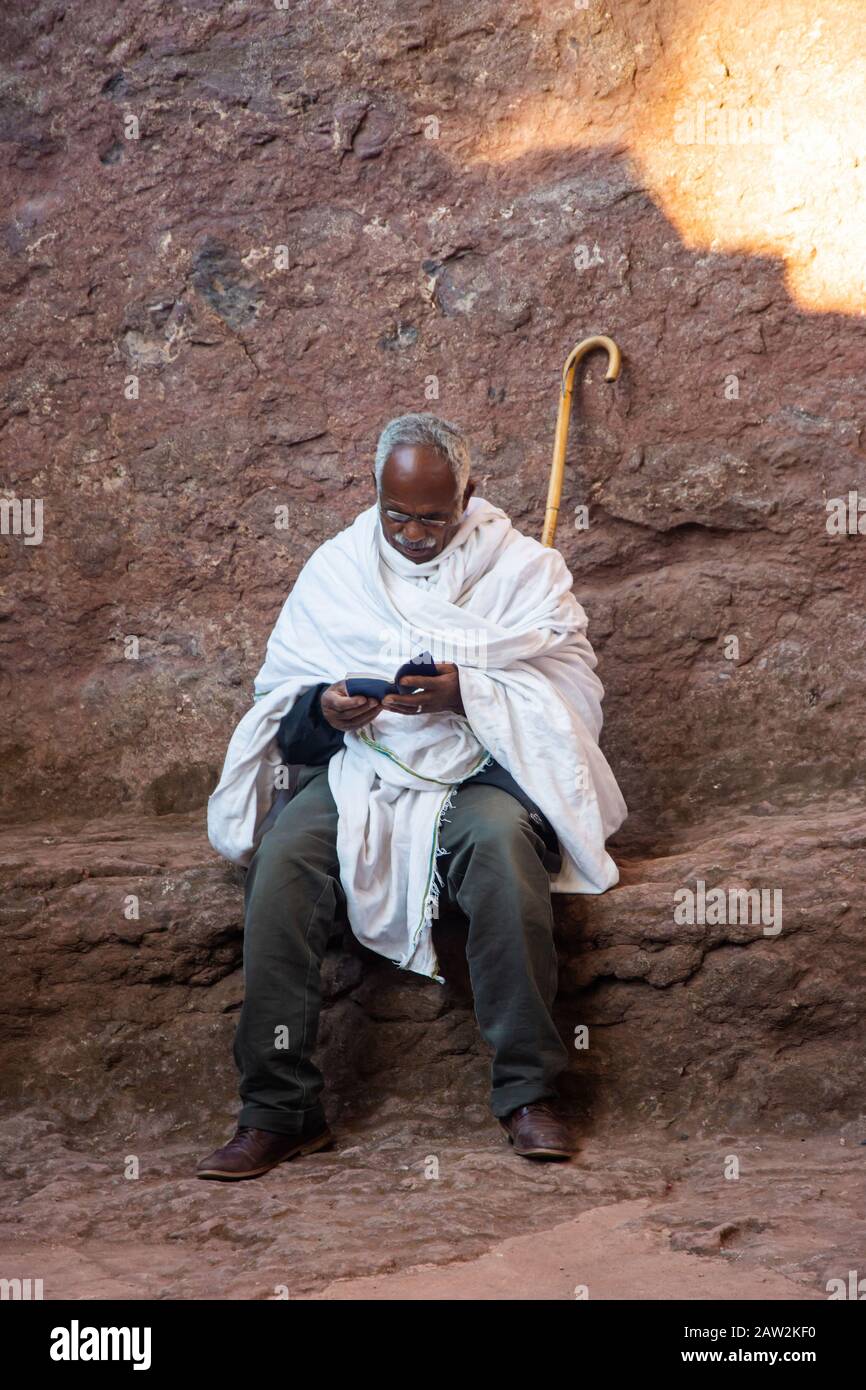 Lalibela, Ethiopie - Nov 2018: Homme vêtu de blanc traditionnel, assis à l'extérieur et lire livre de prières à côté des églises souterraines de Lalibela Banque D'Images