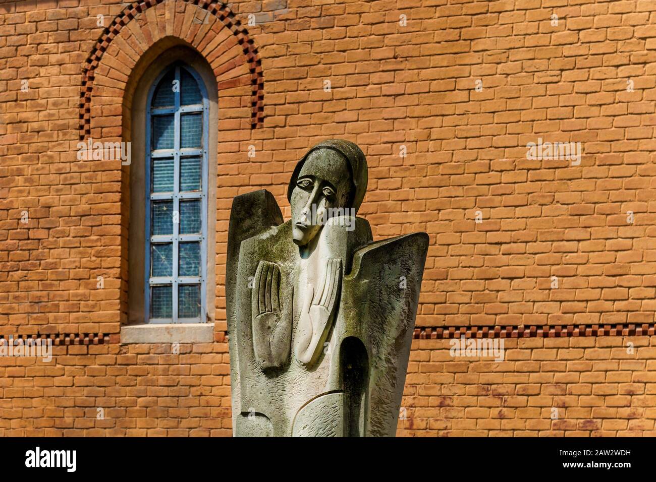 Une ancienne statue religieuse de pleurer la femme sur le fond de la façade de brique de bâtiment un jour ensoleillé. Banque D'Images