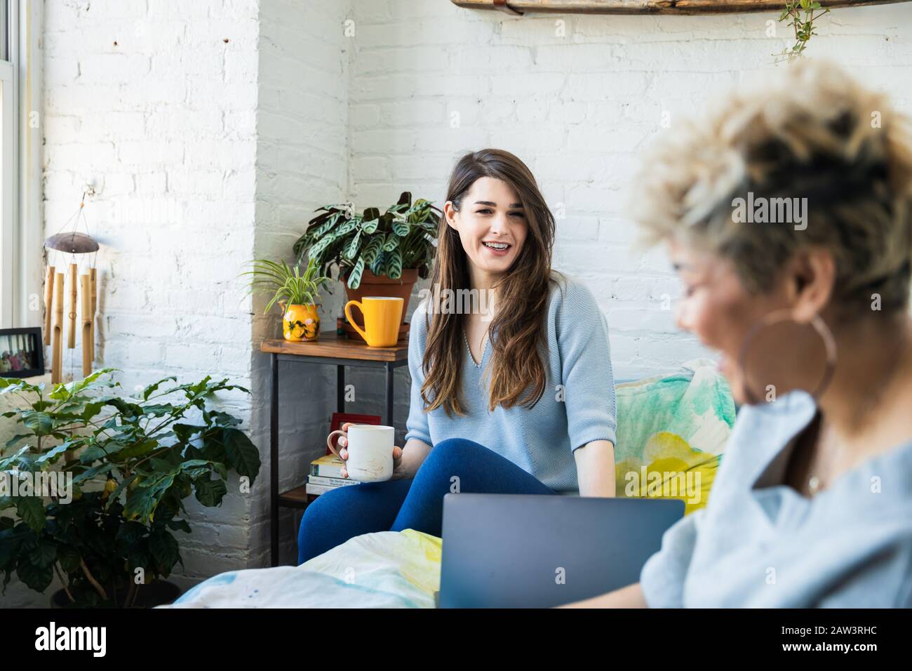 Jeune femme souriante parlant à un ami tout en assis sur le lit à la maison Banque D'Images