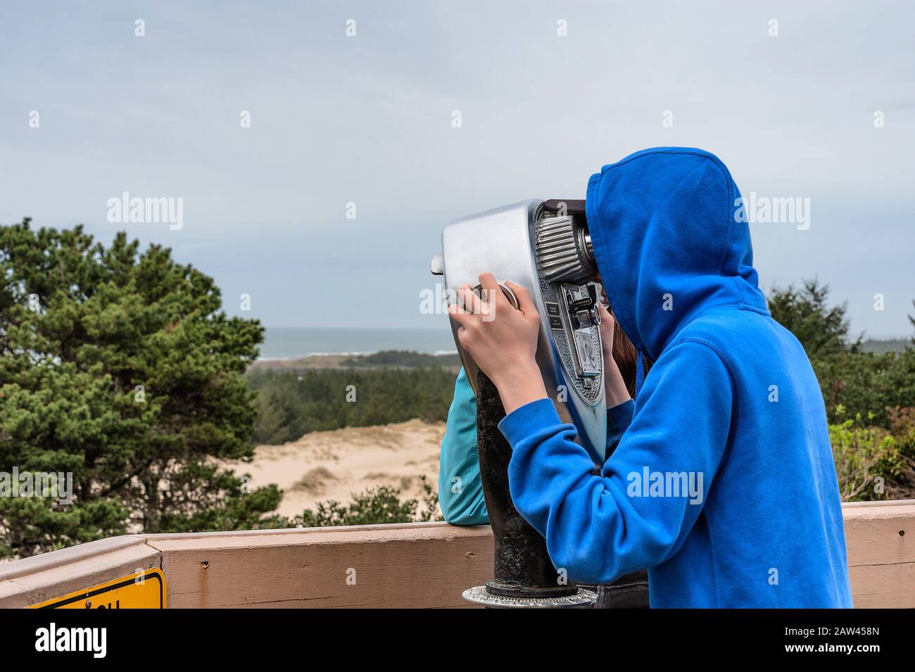 Sur la côte de l'Oregon près de Florence, un jeune adolescent regarde à travers un télescope la vue sur le paysage de la côte. Banque D'Images