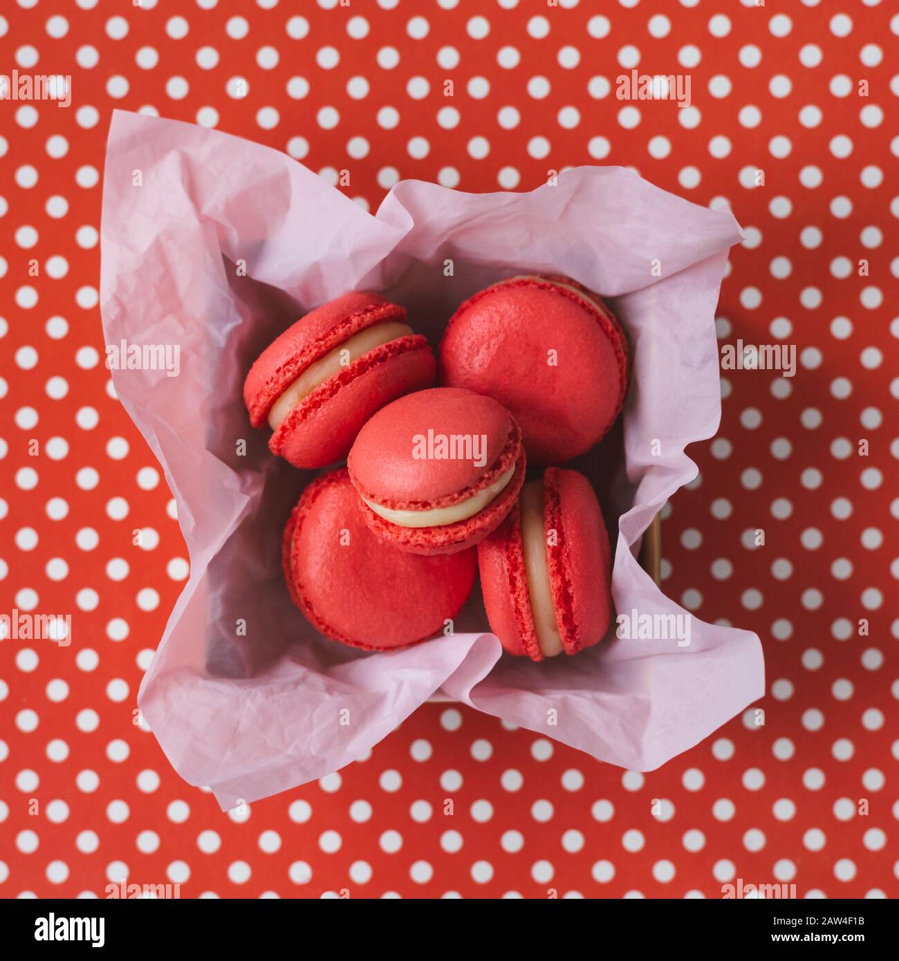 Macarons français rouges dans une boîte sur un fond rouge à pois blancs . Concept pour la Saint-Valentin. Placer pour le texte. Pose plate. Banque D'Images