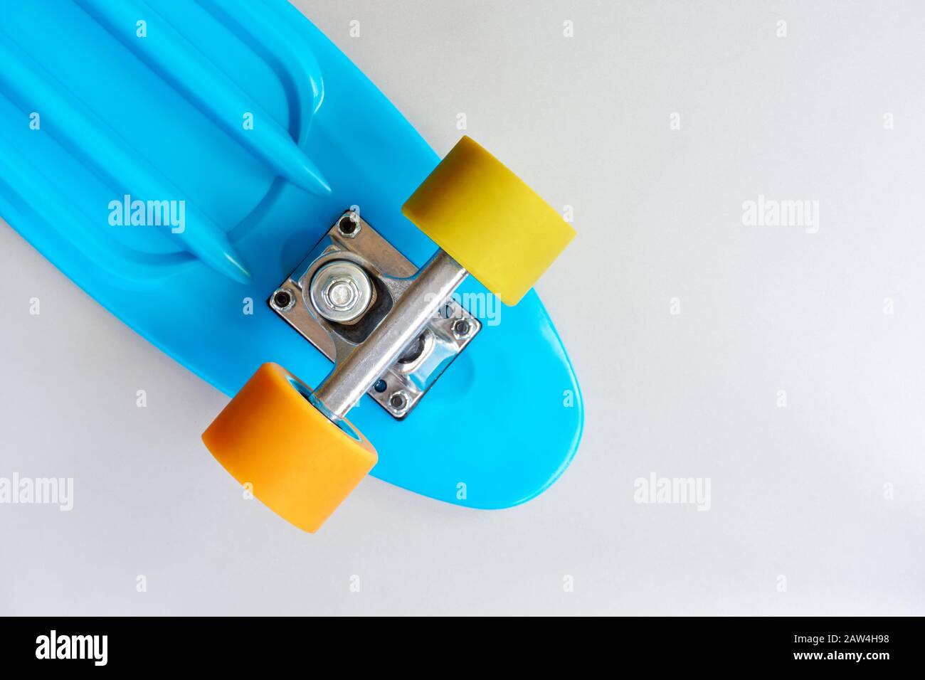 Détail de mini-pension ou de planche à roulettes en plastique bleu avec roues jaune et orange et fixation en métal sur fond gris clair. Banque D'Images