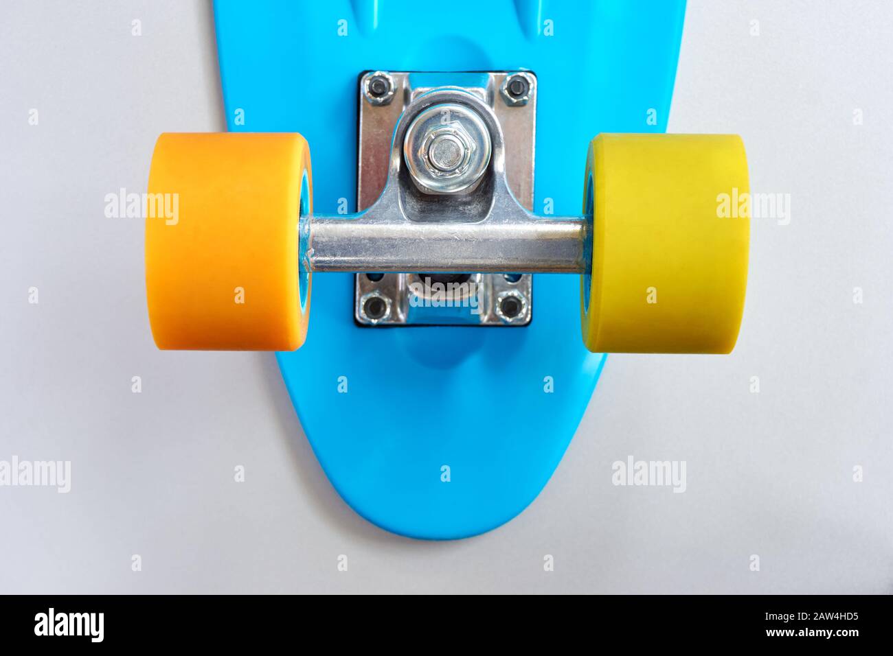 Détail de mini-pension ou de planche à roulettes en plastique bleu avec roues jaune et orange et fixation en métal sur fond gris clair. Banque D'Images