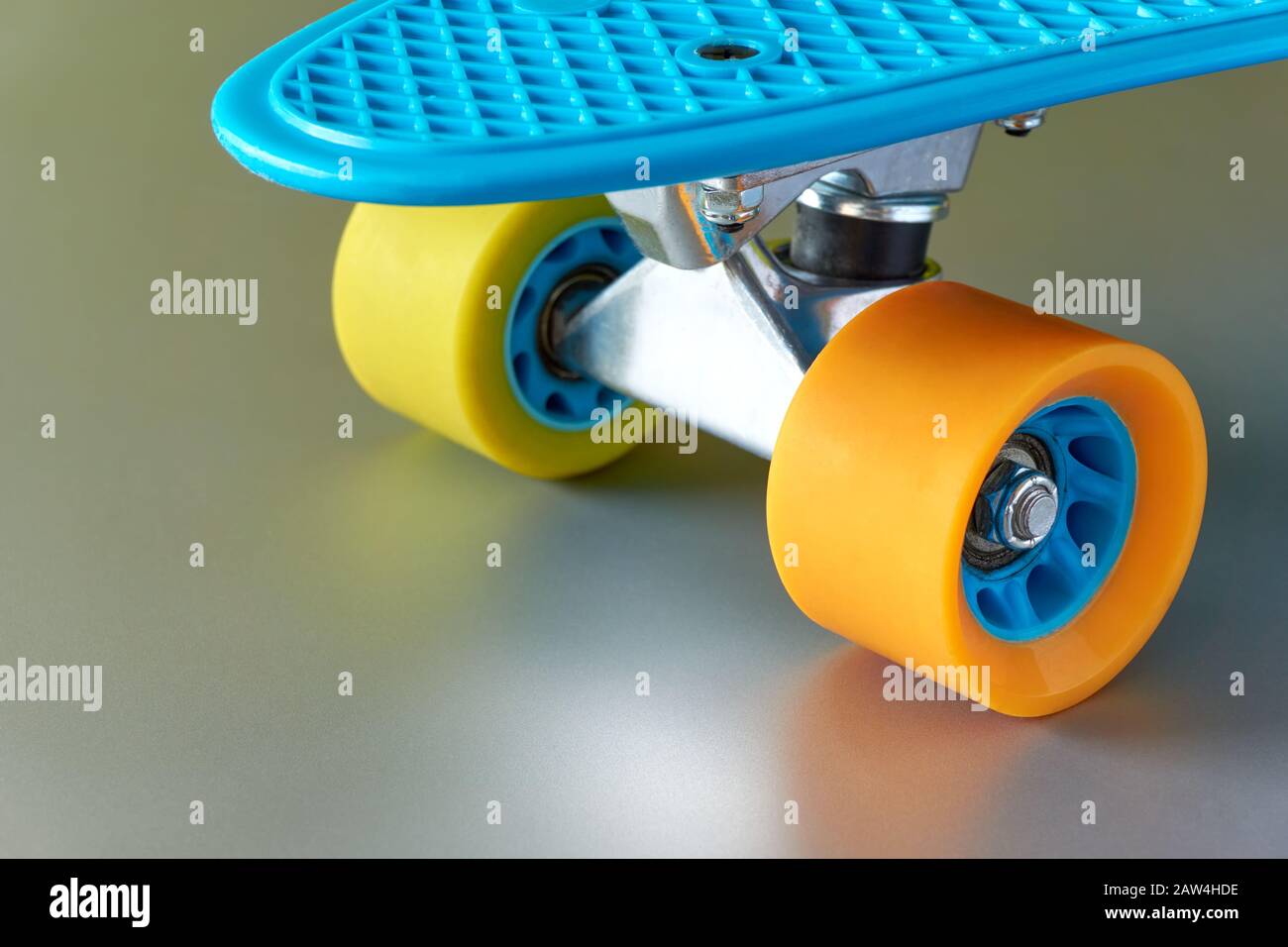 Détail de mini-pension ou de planche à roulettes en plastique bleu avec roues jaunes et orange et fixation en métal sur fond gris métal brillant. Banque D'Images