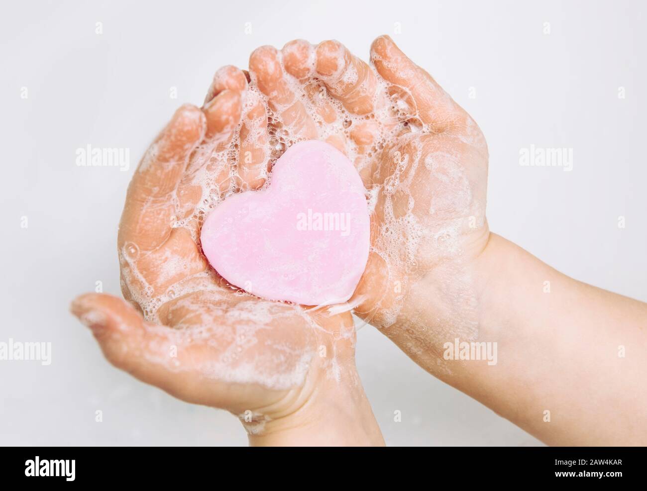 Importance des soins d'hygiène personnelle. Vue plate sur la couche de savon pour enfants se lavant les mains sales avec une barre de savon rose en forme de coeur, beaucoup de mousse. Espace de copie. Banque D'Images