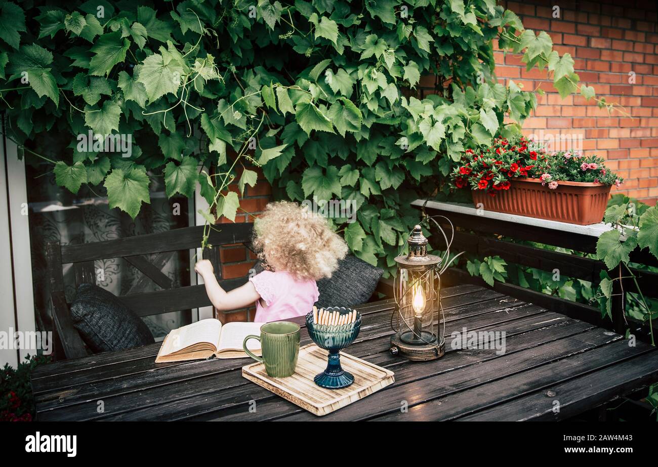 Balcon privé à l'extérieur avec des vignes décoratives grimpant sur le mur, meubles de jardin en bois brun, tasse à boire, biscuits et jeu d'enfant avec raisin v Banque D'Images