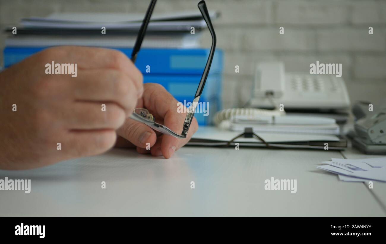 Homme d'affaires Assis sur le bureau dans son bureau et Gardant les lunettes de vue Dans Les Mains Banque D'Images