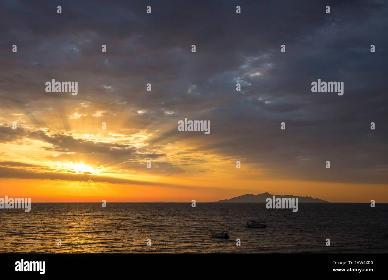 Lever du soleil depuis la mer Égée, rayons de soleil magiques qui brillent dans les nuages, silhouette d'île volcanique (Anafi, Grèce, vue de l'île de Santorin) sur le bac Banque D'Images