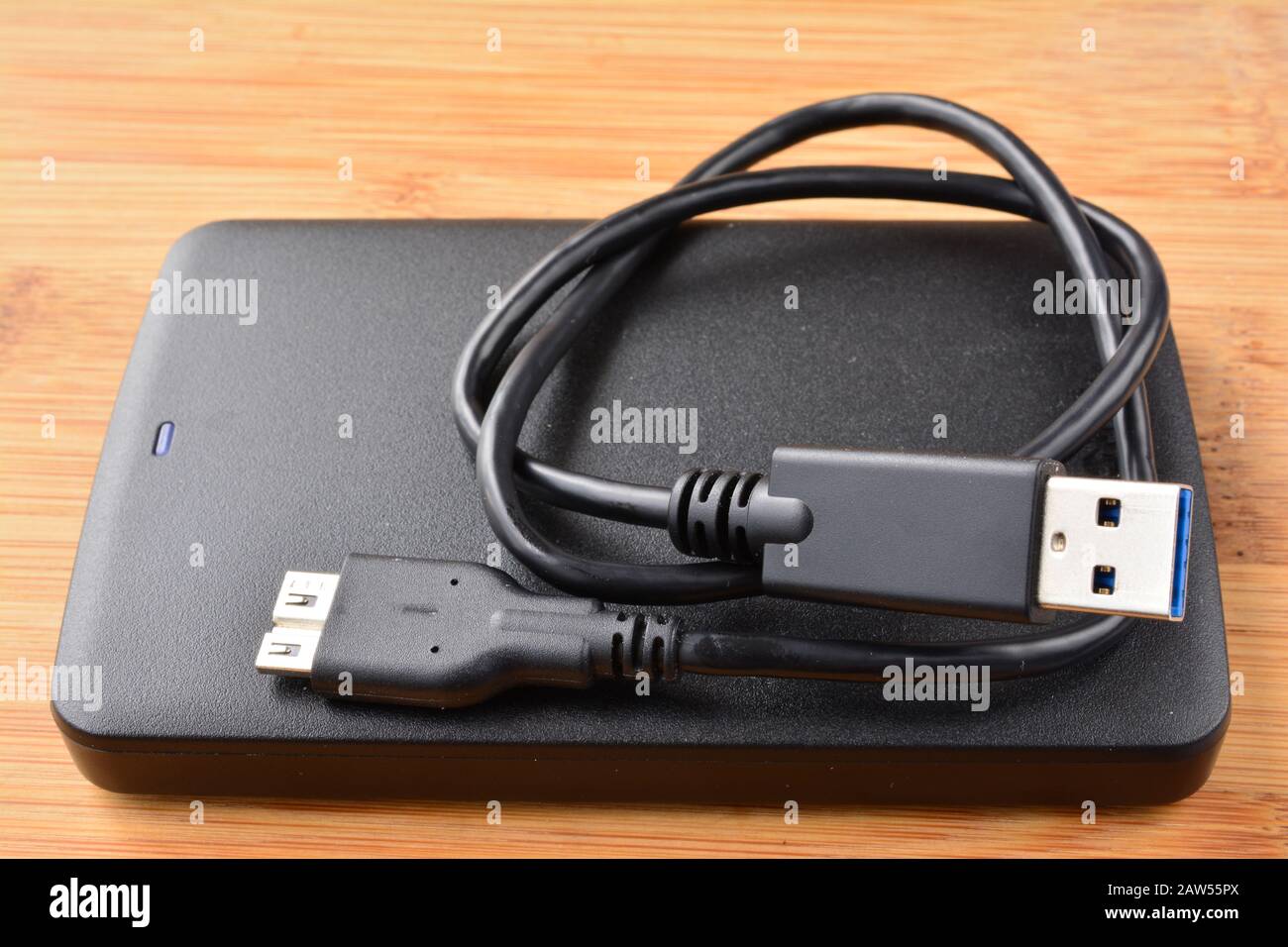 Disque dur USB 3.0 externe noir et plat avec câble USB 3.0 enroulé sur fond en bois, vue latérale Banque D'Images