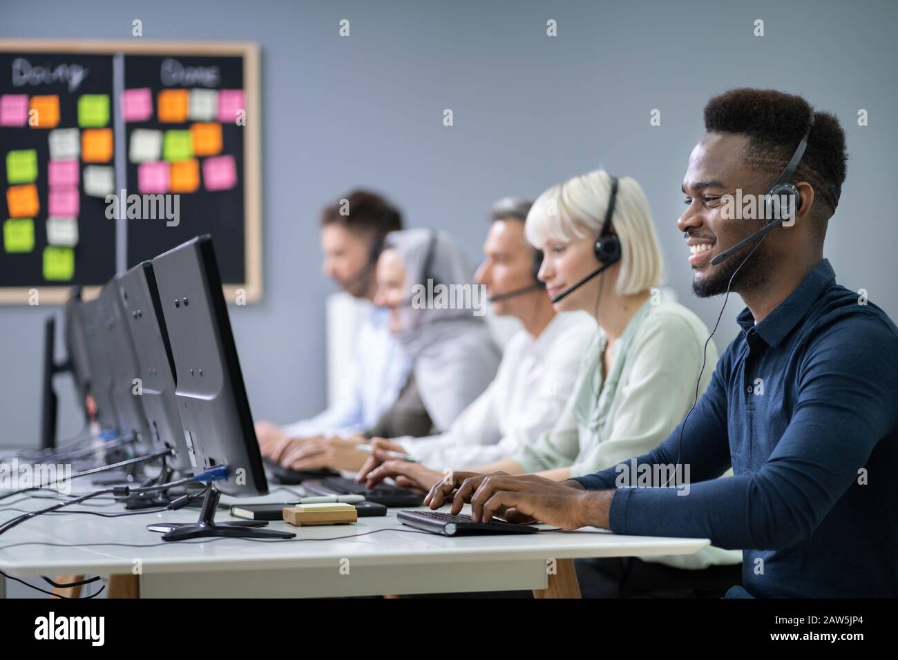 L'agent des services à la clientèle masculine positive avec casque de travail dans un centre d'appels Banque D'Images