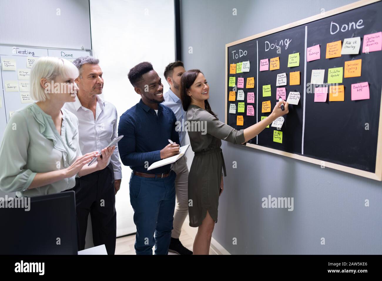 Vue Latérale Du Groupe De Personnes Écrivant Sur Des Notes Adhésives Jointes À Blackboard Au Bureau Banque D'Images