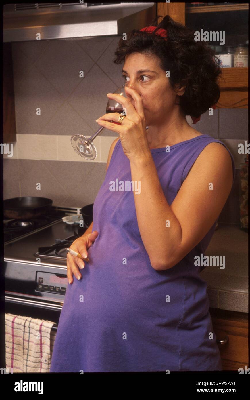 La femme enceinte se détend tout en buvant du vin et en fumant une cigarette chez elle à Austin, au Texas. Banque D'Images