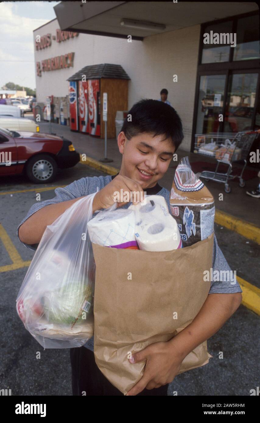 Un adolescent hispanique quitte une épicerie à Austin, au Texas, avec des sacs complets de nourriture et de fournitures ménagères. Banque D'Images