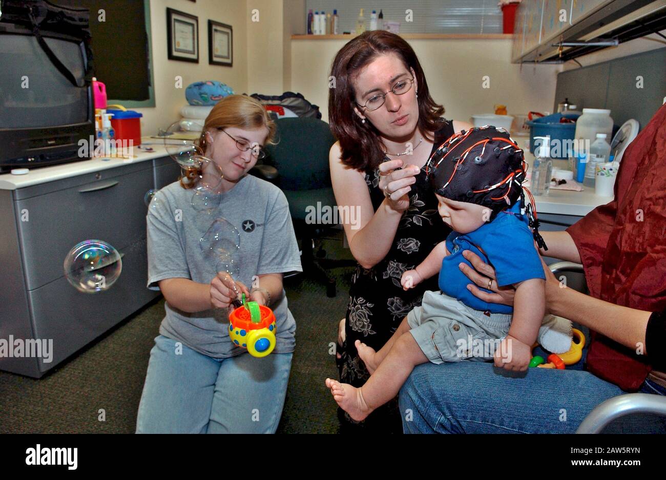 La chercheuse féminine met le cap EEG sur 6 mois lors d'une étude sur la capacité de reconnaissance des parents par l'activité de la vague cérébrale alors que la mère le maintient sur ses genoux. Banque D'Images