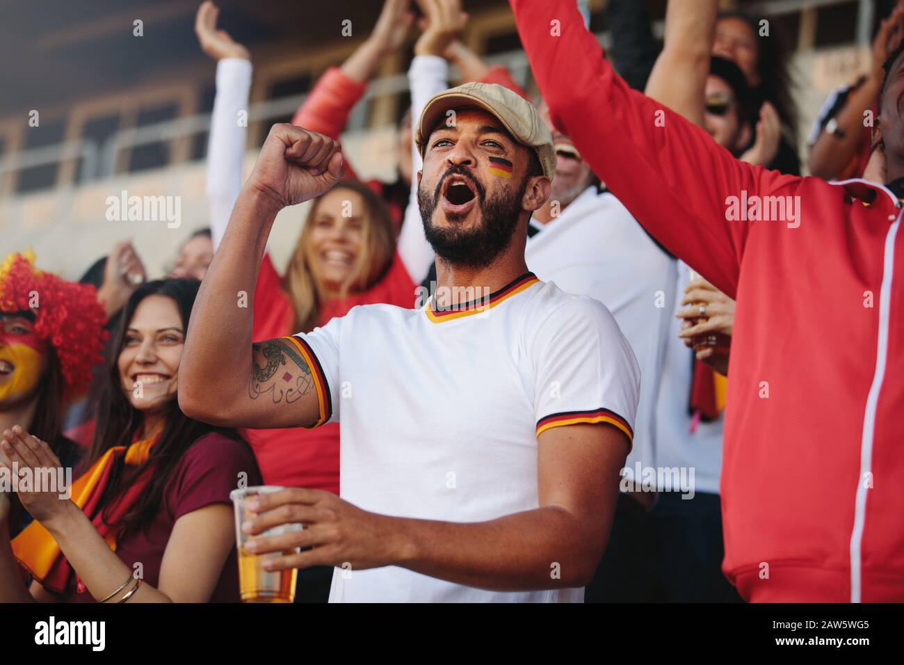 Foule de spectateurs qui applaudissaient à un événement sportif, avec un homme qui tient un verre de bière. Les supporters de l'équipe de football allemande chantent activement dans le stade. Banque D'Images