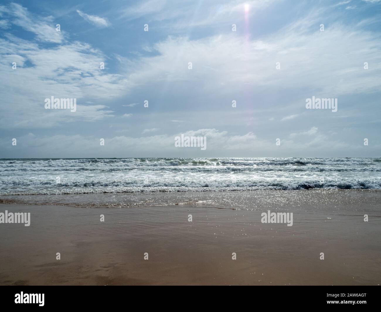 Vagues se déroulant sur la rive et le soleil qui brillent à travers les nuages, sable humide étincelant, plage australienne Banque D'Images