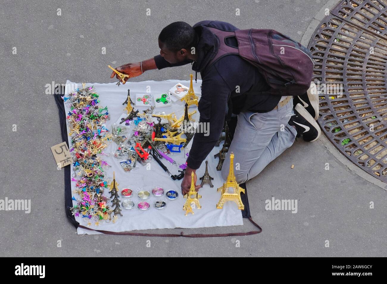 Un vendeur de rue illégal vendant des souvenirs multicolores de la Tour Eiffel à Paris agenouillé sur un tissu ouvert qui se transforme en sac de transport Banque D'Images