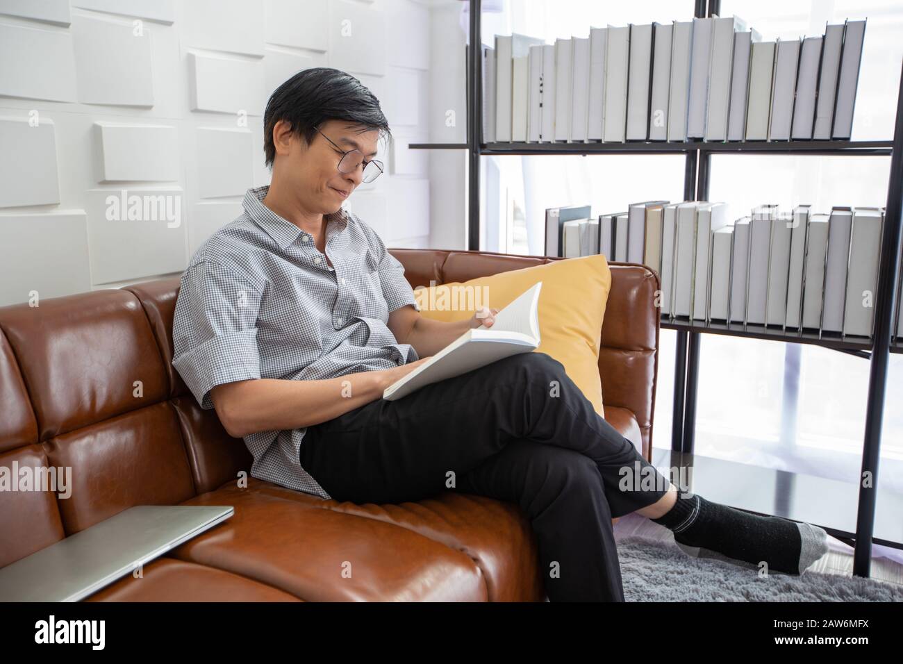 Livre de lecture de l'homme asiatique senior sur le canapé dans le salon à la maison, Portrait de l'homme asiatique âgé est Relaxant et bonheur Avec Read a Magazine Banque D'Images