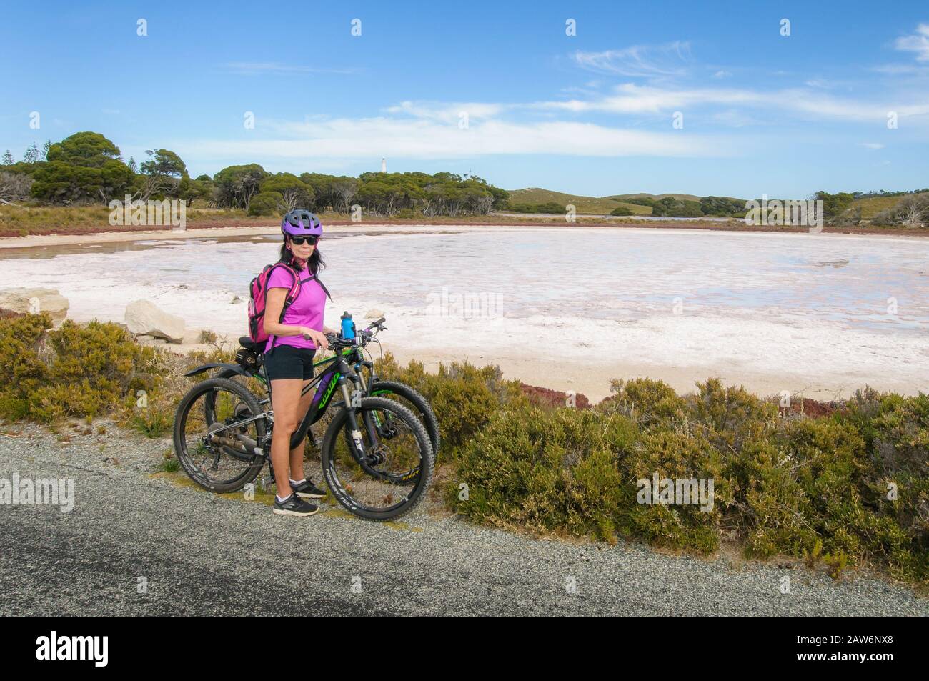Un cycliste pose dans un chemisier rose chaud devant le lac Pink sur l'île Rottnest Banque D'Images