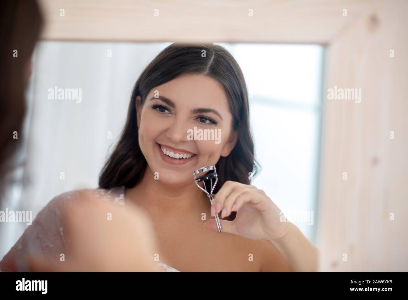 Jeune femme assez pleine-figurée curling ses cils Banque D'Images