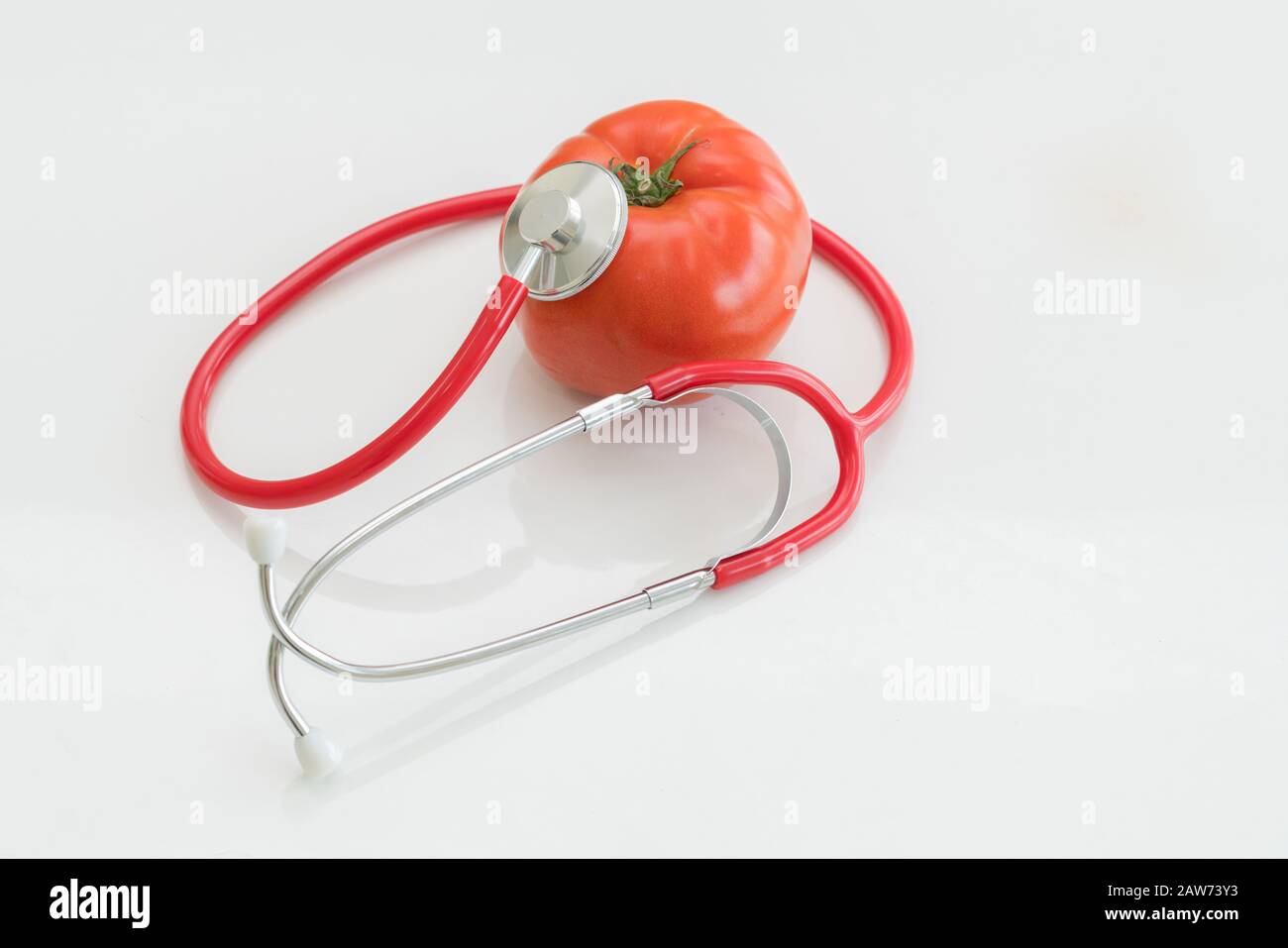 Concept d'aliments sains - tomate et médecin stéthoscope sur fonds blancs montrant les avantages de la vitamine et des nutriments de la tomate. Banque D'Images
