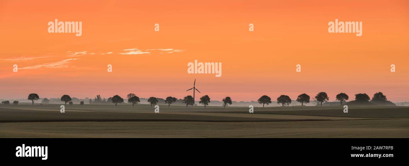 Lever du soleil, éolienne et ligne de soutien dans le paysage rural à Soderslatt, Skane, Suède, Scandinavie. Banque D'Images