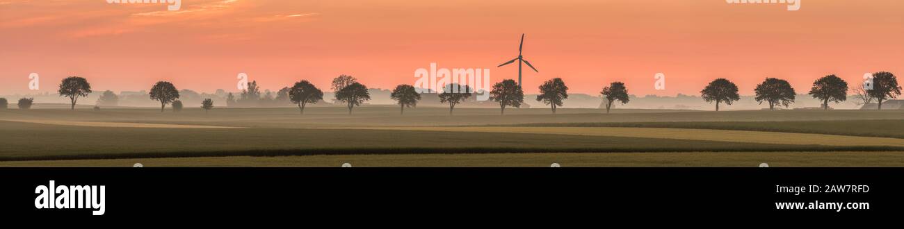 Lever du soleil, éolienne et ligne de soutien dans le paysage rural à Soderslatt, Skane, Suède, Scandinavie. Banque D'Images