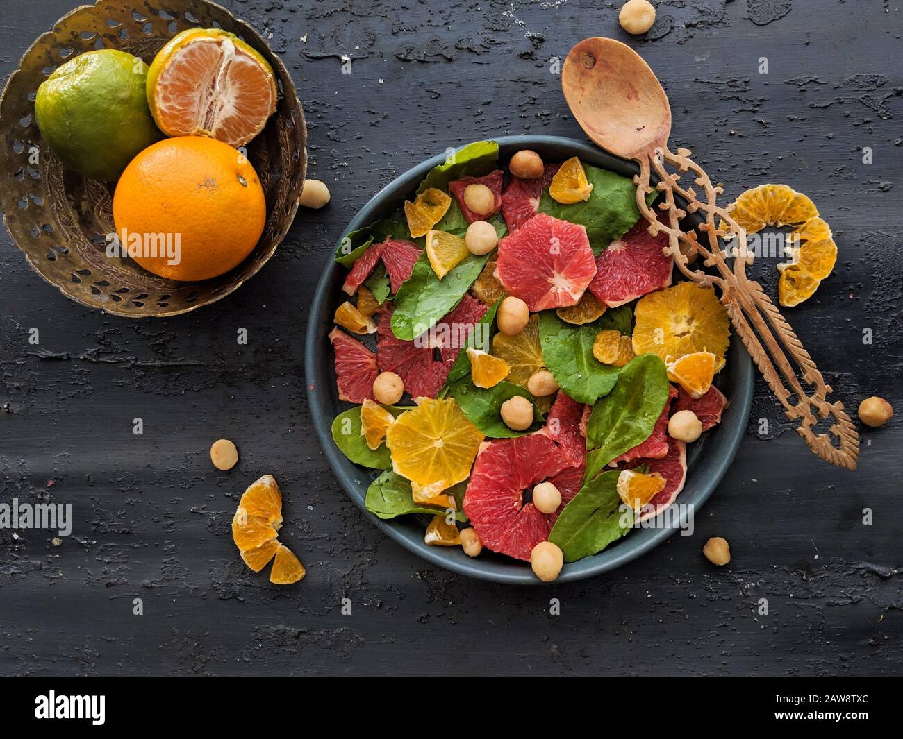 Vue de dessus de salade d'agrumes, avec feuilles d'épinards et noisettes dans un plat noir avec une cuillère en bois. Mélange de fruits tropicaux, citron vert, café Banque D'Images