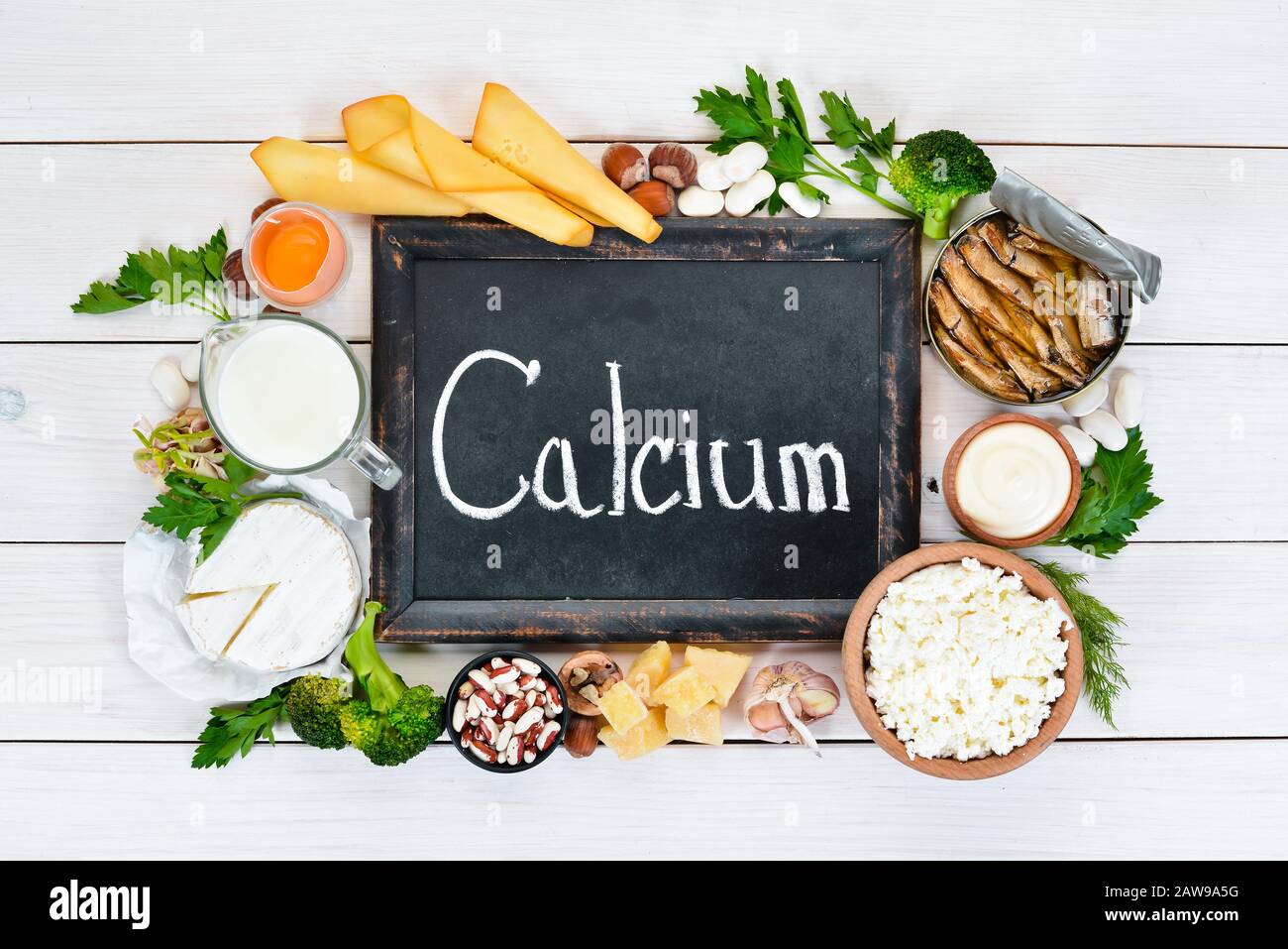 Nourriture avec calcium. Une variété d'aliments riches en calcium :  fromage, lait, parmesan, crème sure, poisson, amandes, persil, ail,  brocoli. Sur un bois blanc Photo Stock - Alamy