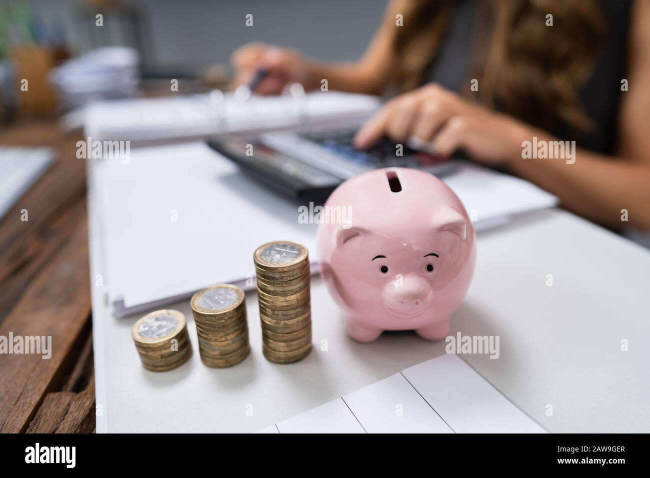 Femme D'Affaires Utilisant Calculatrice Avec Piggybank Et Pile De Pièces Sur Le Bureau Banque D'Images