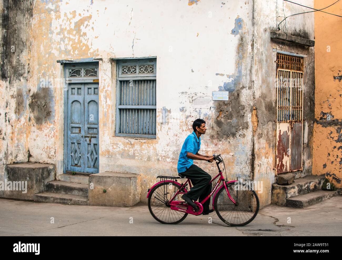 Un homme passe à vélo devant les murs en décomposition et les portes en bois pittoresques et les fenêtres des vieilles maisons dans les rues de l'île De Diu en Inde. Banque D'Images