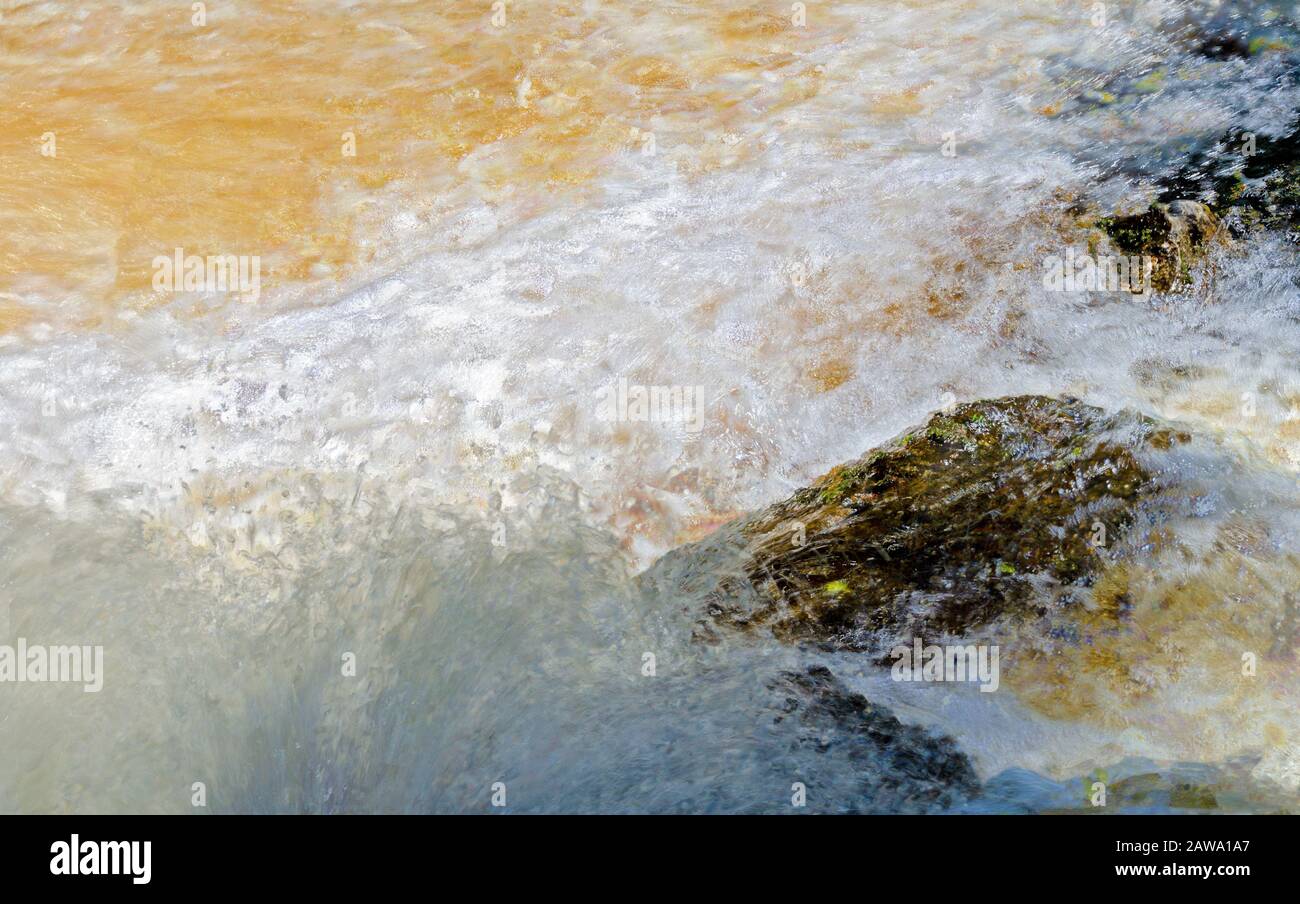 Mousse et éclaboussures d'eau blanche de couleur or débordant de roches en Suède Banque D'Images
