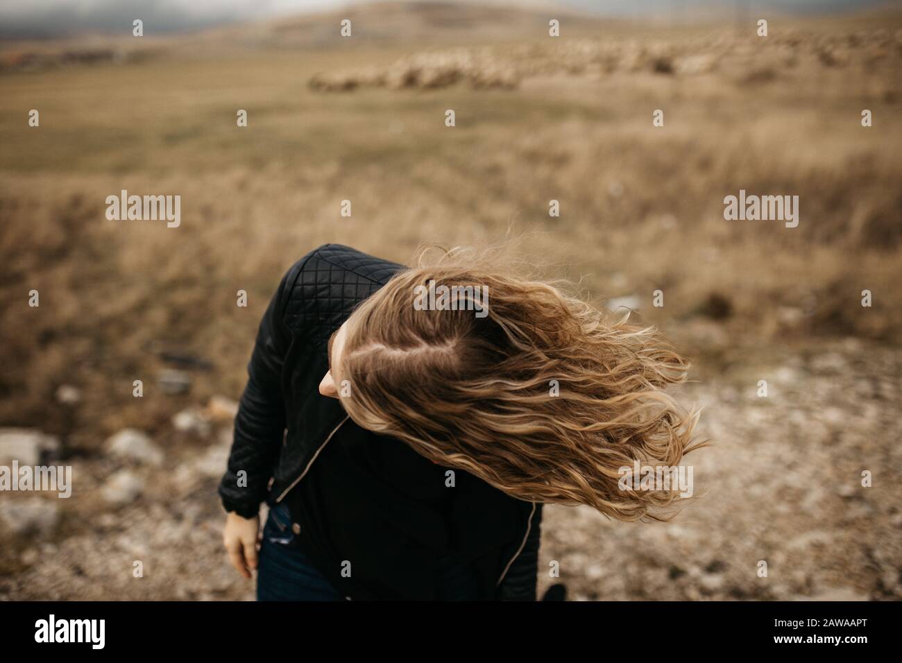 Portrait de la jeune femme avec des cheveux soufflant dans le vent. Elle porte une veste en cuir avec une nature et une route floues en arrière-plan. Banque D'Images