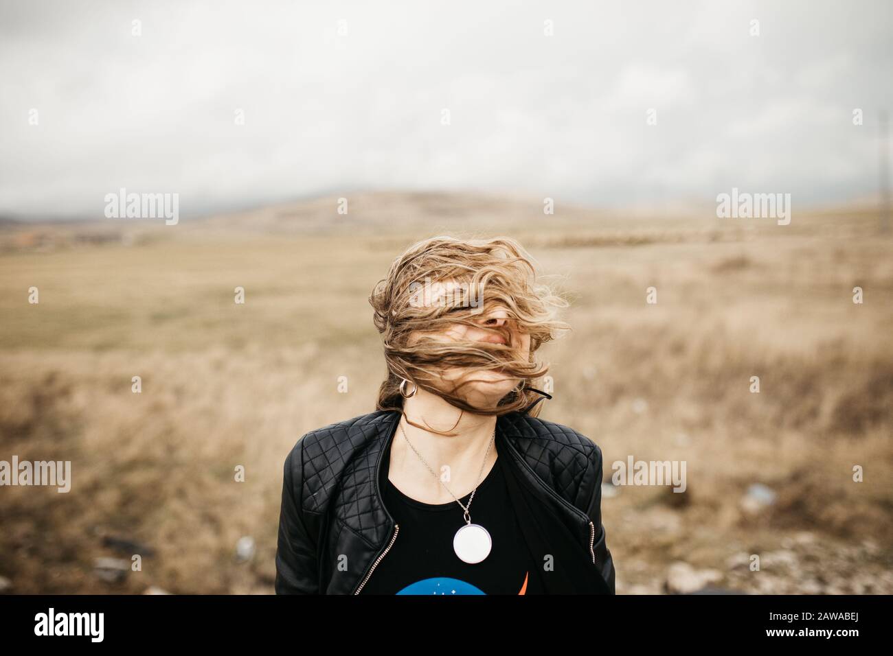 Portrait de la jeune femme avec des cheveux soufflant dans le vent. Elle porte une veste en cuir avec une nature et une route floues en arrière-plan. Banque D'Images