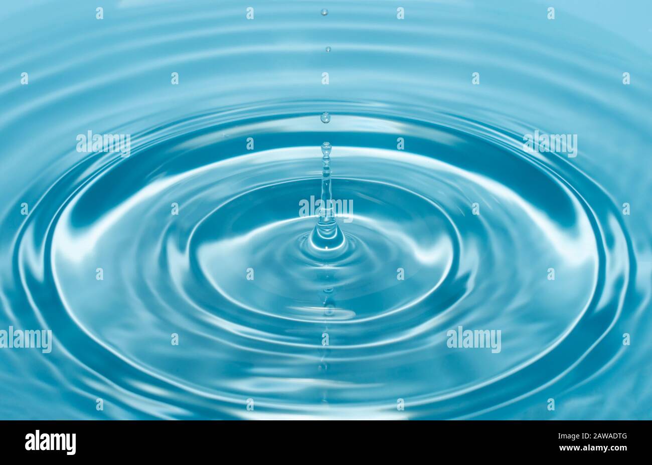 une goutte d'eau tombe avec un jet dans l'eau claire et bleue formant des cercles sur l'eau. Banque D'Images