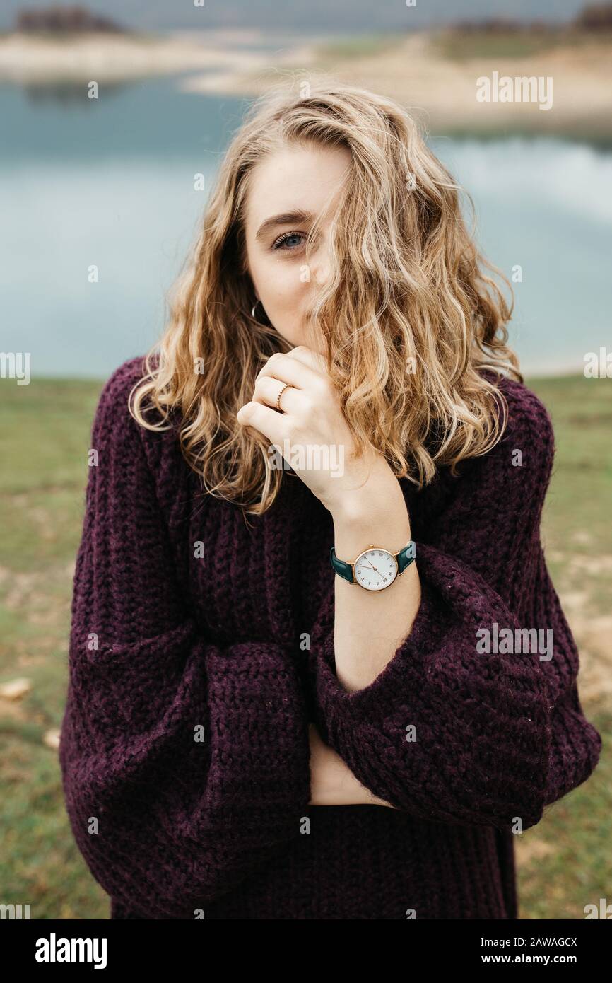 Portrait extérieur de la jeune femme avec des cheveux bouclés portant une montre tendance au poignet. Elle se tient près du lac. Banque D'Images