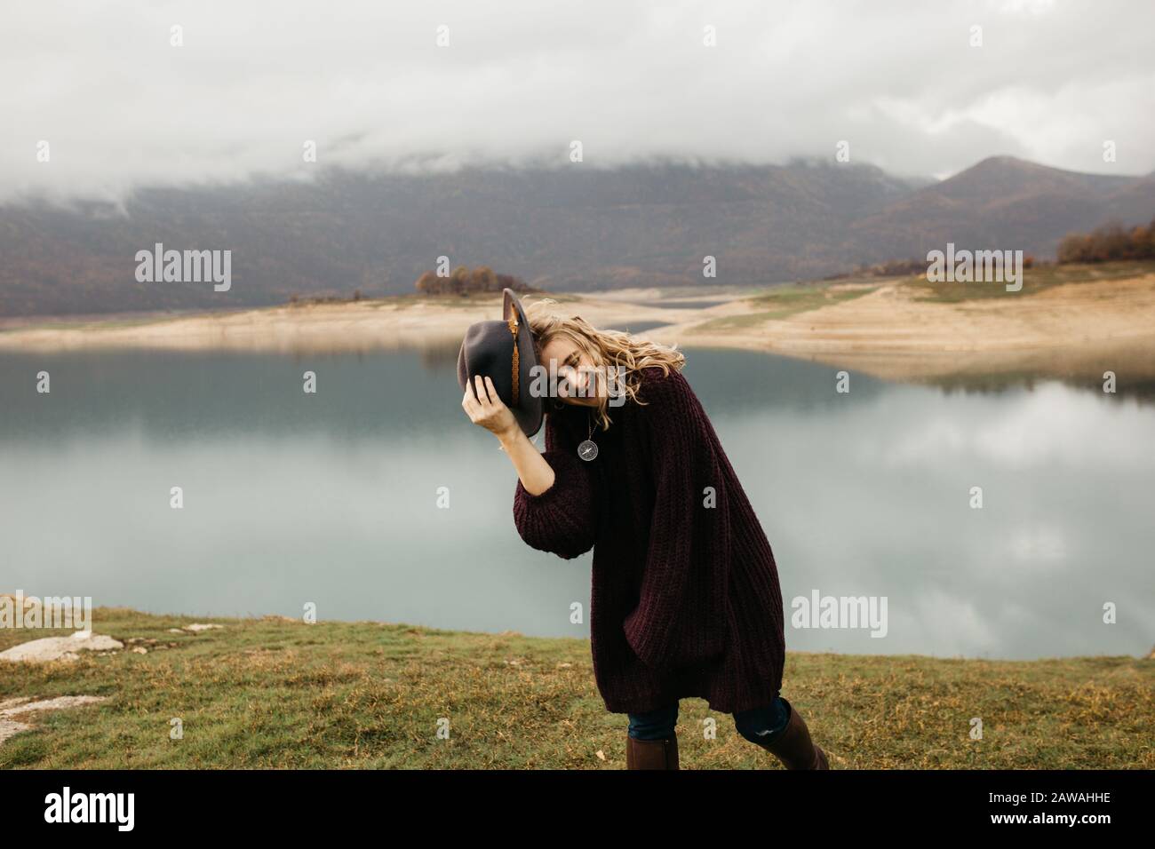 Heureuse belle femme en sweat-shirt violet tenant son chapeau et en profitant de voyage sur le lac. Tourisme explorer le lac. Elle souriait et attrape son chapeau. Banque D'Images