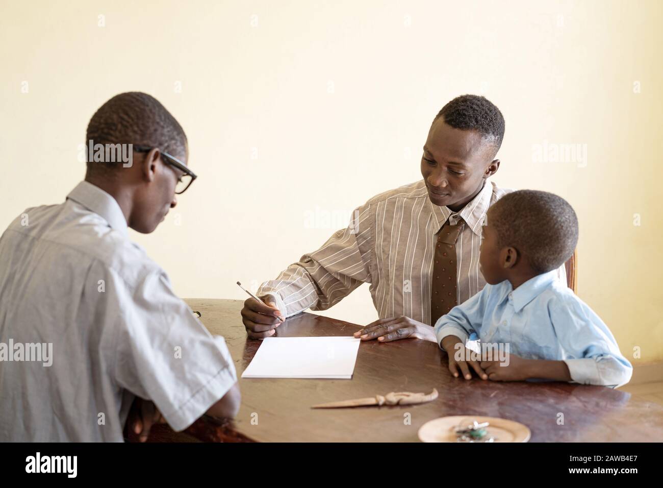 Père africain avec son fils s'appliquant à l'école avec le directeur de l'école en signant un contrat dans un bureau Banque D'Images