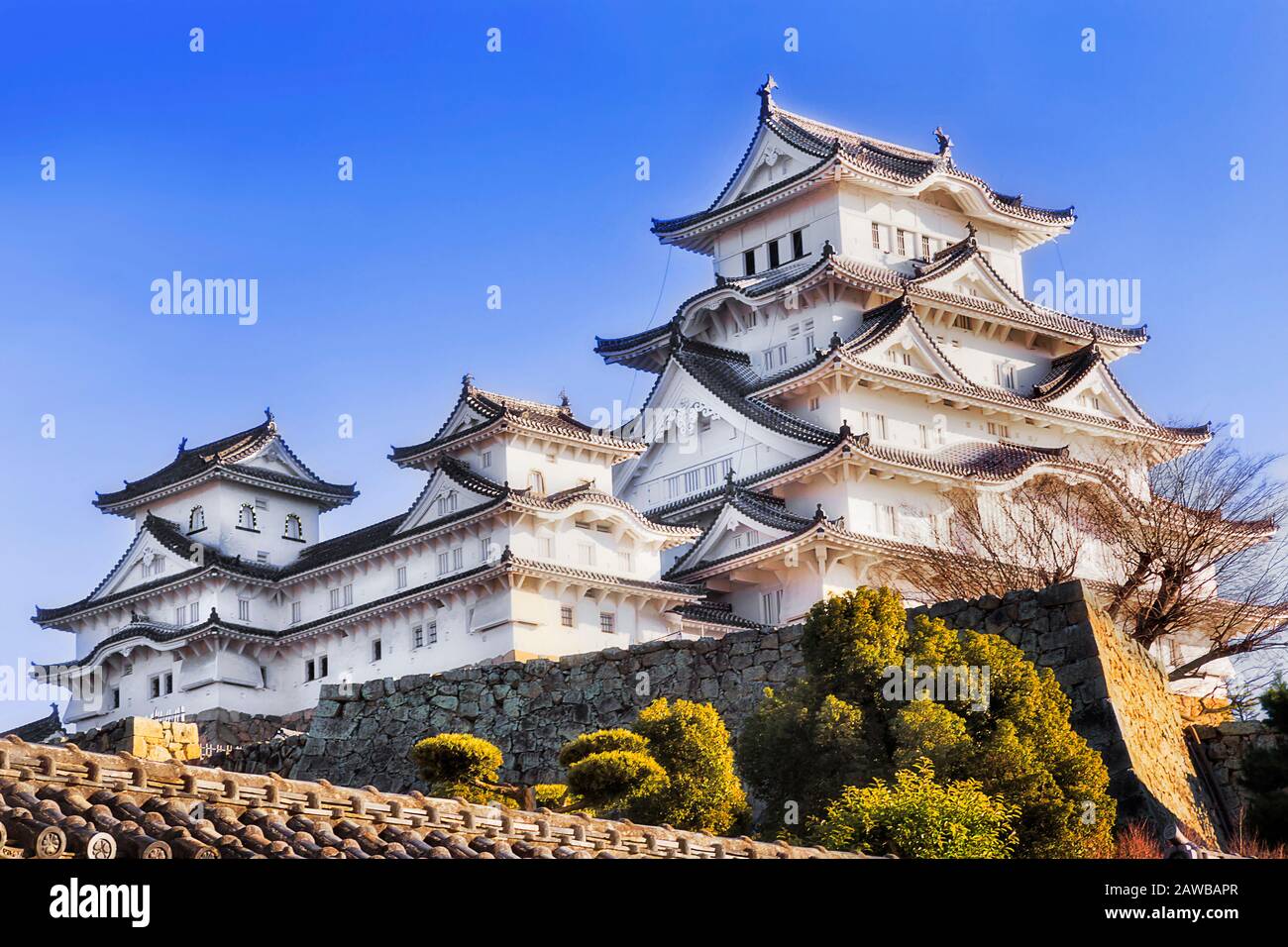 Château historique peint en blanc dans la ville japonaise Himeji au-dessus des murs en pierre sous le ciel bleu. Banque D'Images
