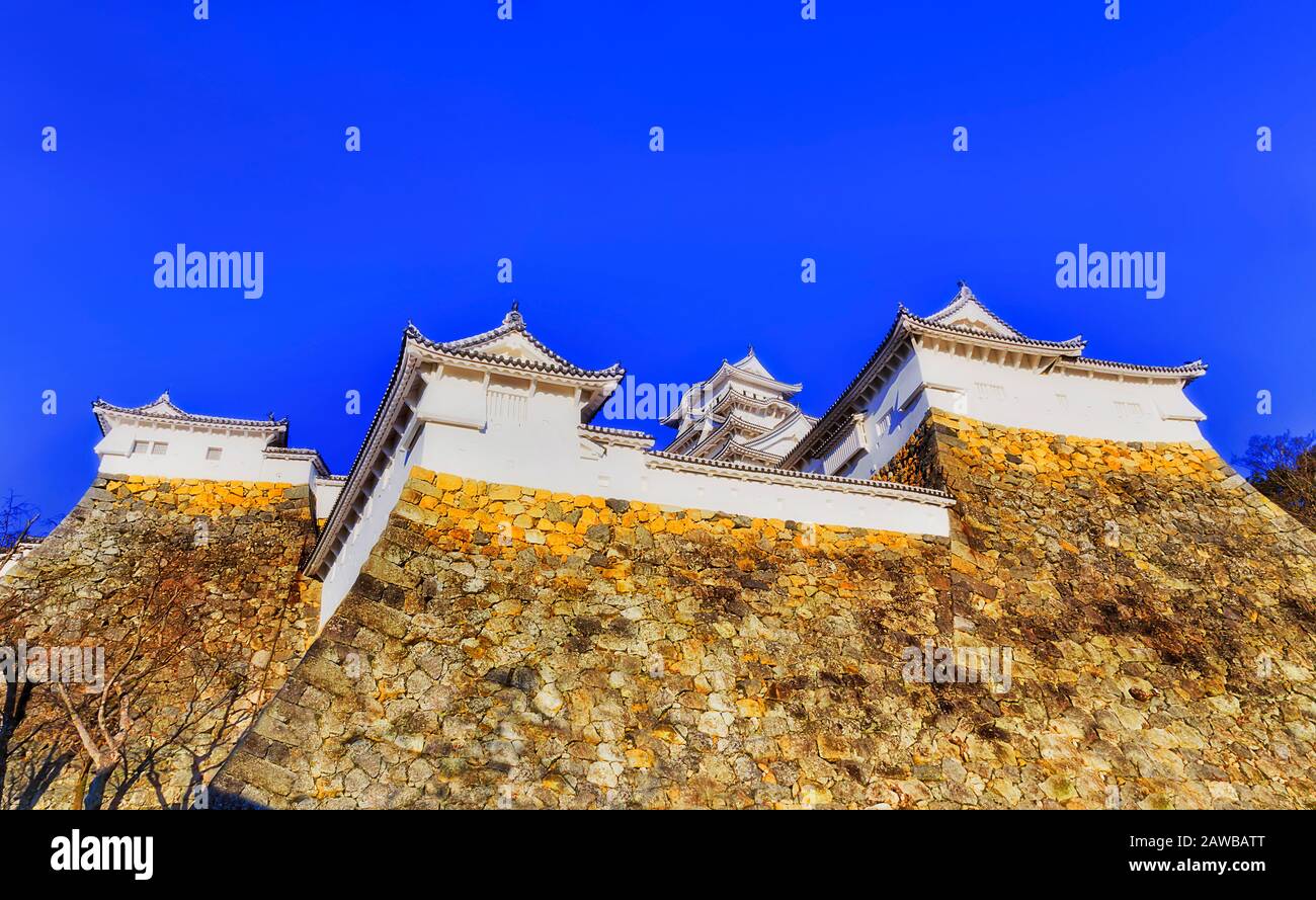 Quatre tours blanches ove de grands murs en pierre du château d'Himeji au Japon sous le ciel bleu clair. Banque D'Images