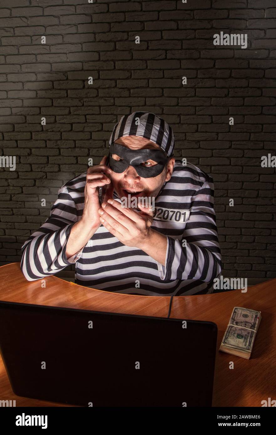 Personnage de bande dessinée prisonnier téléphone con homme assis sur un ordinateur portable dans un peignoir rayé et un chapeau dans un masque noir et tricher sur le téléphone Banque D'Images