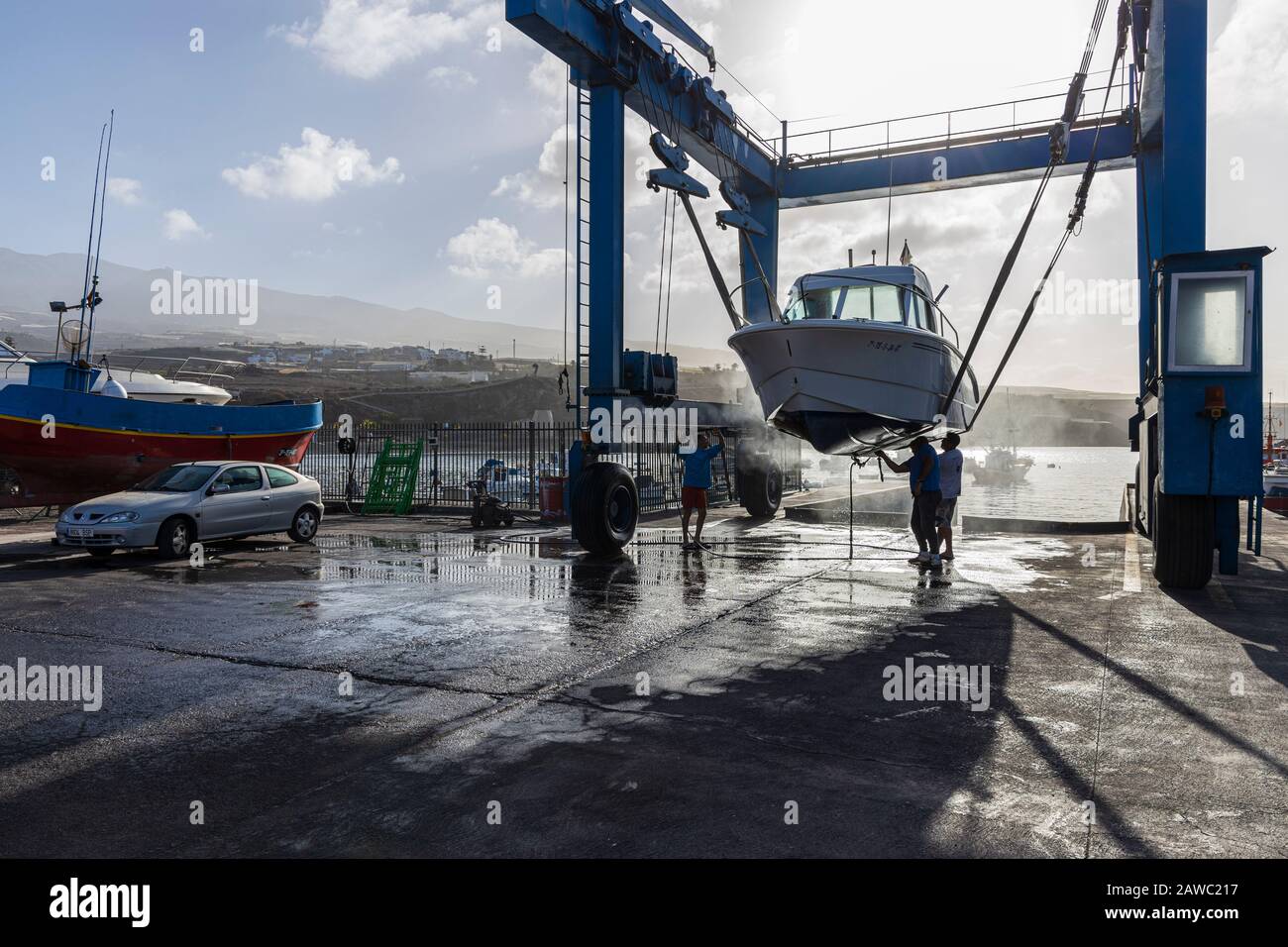 Nettoyage de la coque inférieure d'un bateau suspendu dans une grue de levage dans un quai sec au port de Playa San Juan, Tenerife, îles Canaries, Espagne Banque D'Images