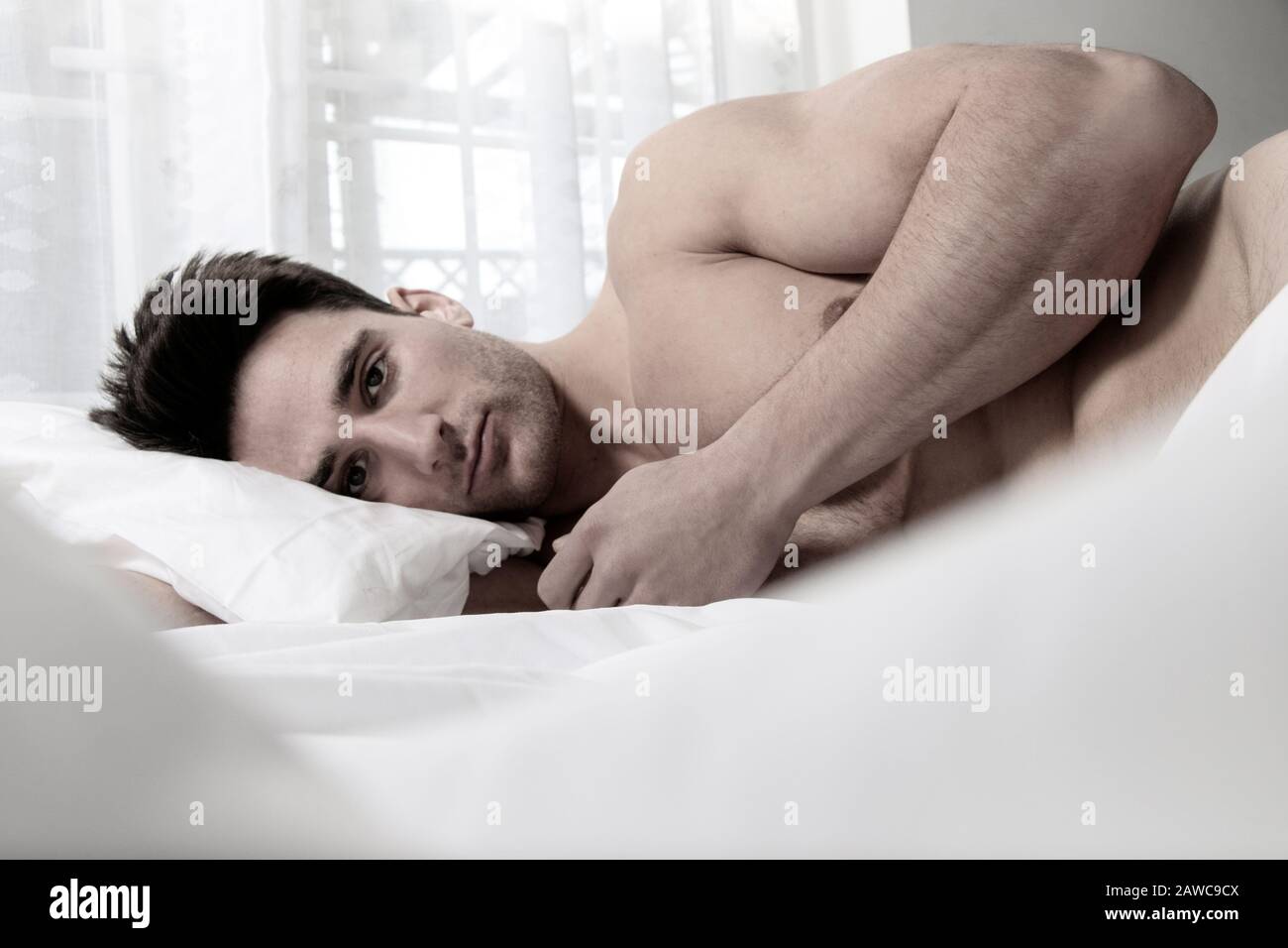 Homme musclé sexy et nu allongé dans un lit recouvert d'une feuille,  regardant l'appareil photo Photo Stock - Alamy
