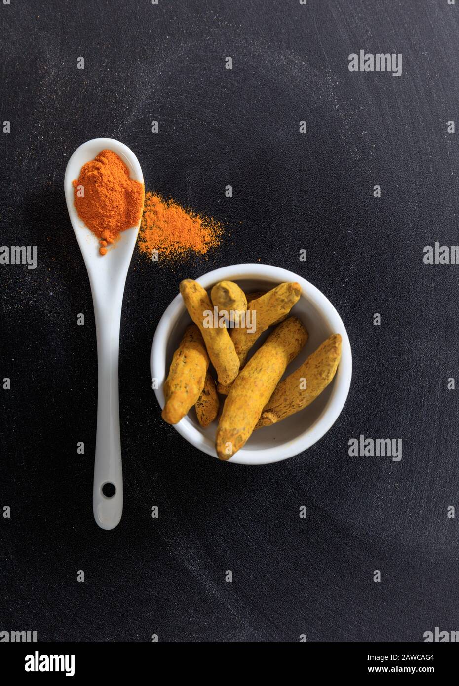 Curcumine curcumine ou curcuma racines et poudre dans un bol et une cuillère en porcelaine, fond noir, vue de dessus Banque D'Images