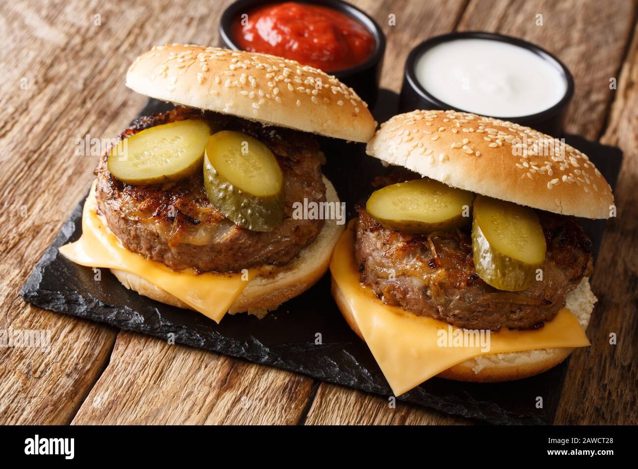 Des hamburgers faits maison à l'oignon frit avec du fromage cheddar et des cornichons se rapprochant sur une planche en ardoise sur une table. Horizontale Banque D'Images